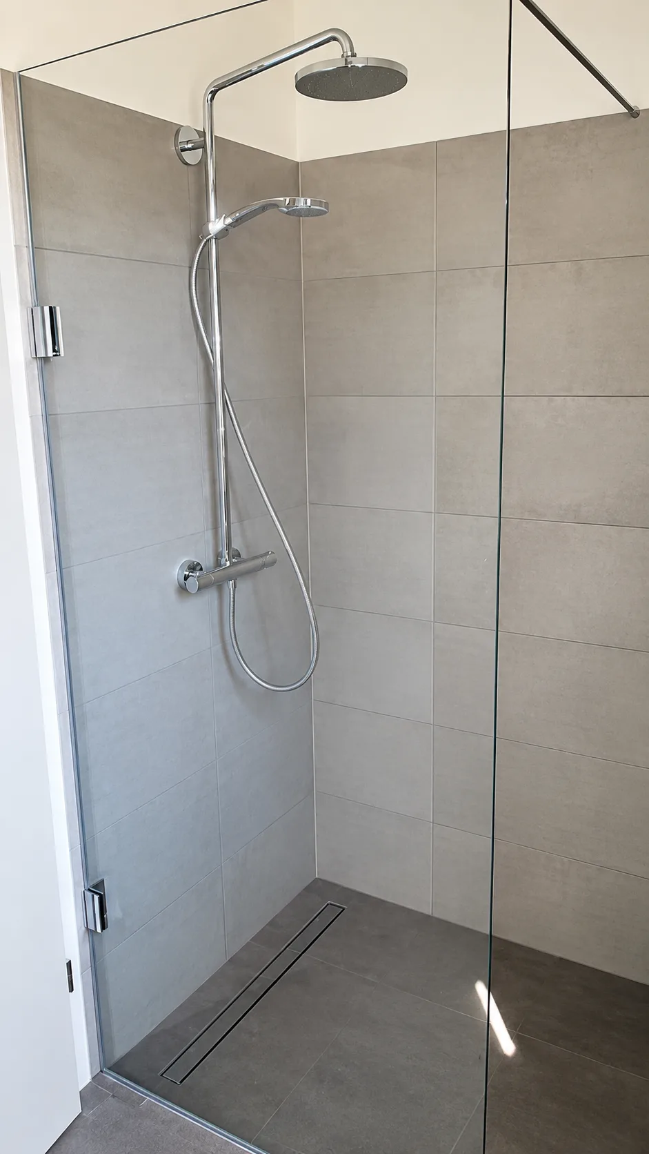 Moderne Glasdusche mit rahmenloser Glasabtrennung und Regenbrause vor grauen Fliesen