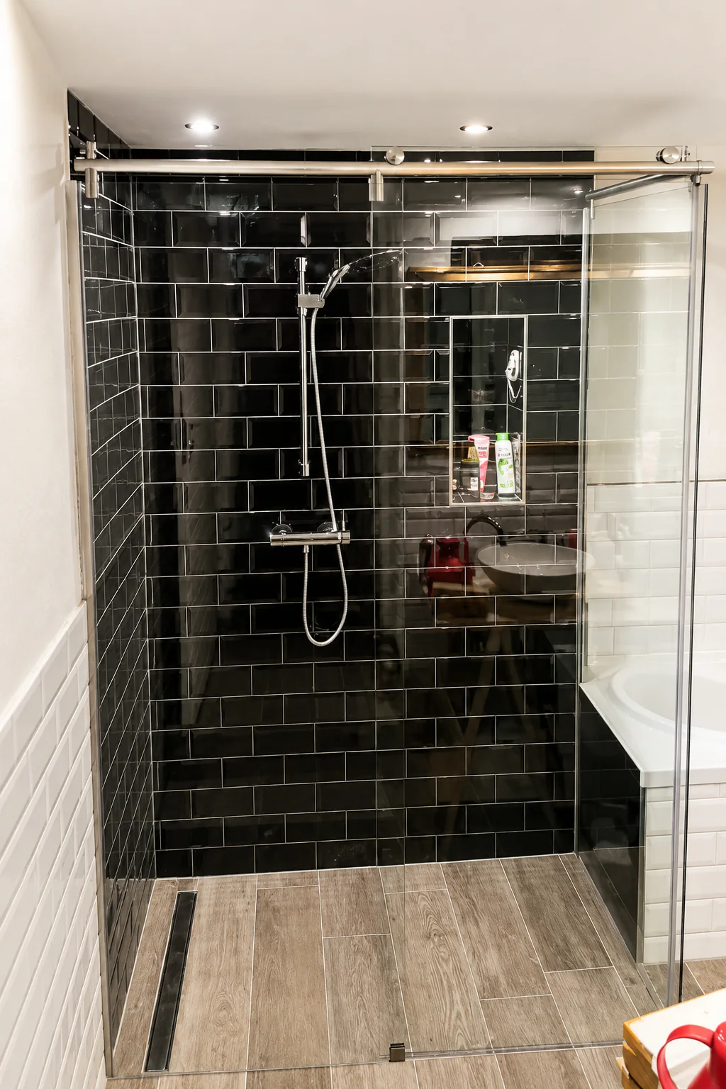 Gesamtansicht einer Dusche mit Glas-Schiebetür vor schwarzen Fliesen, direkt neben der Badewanne