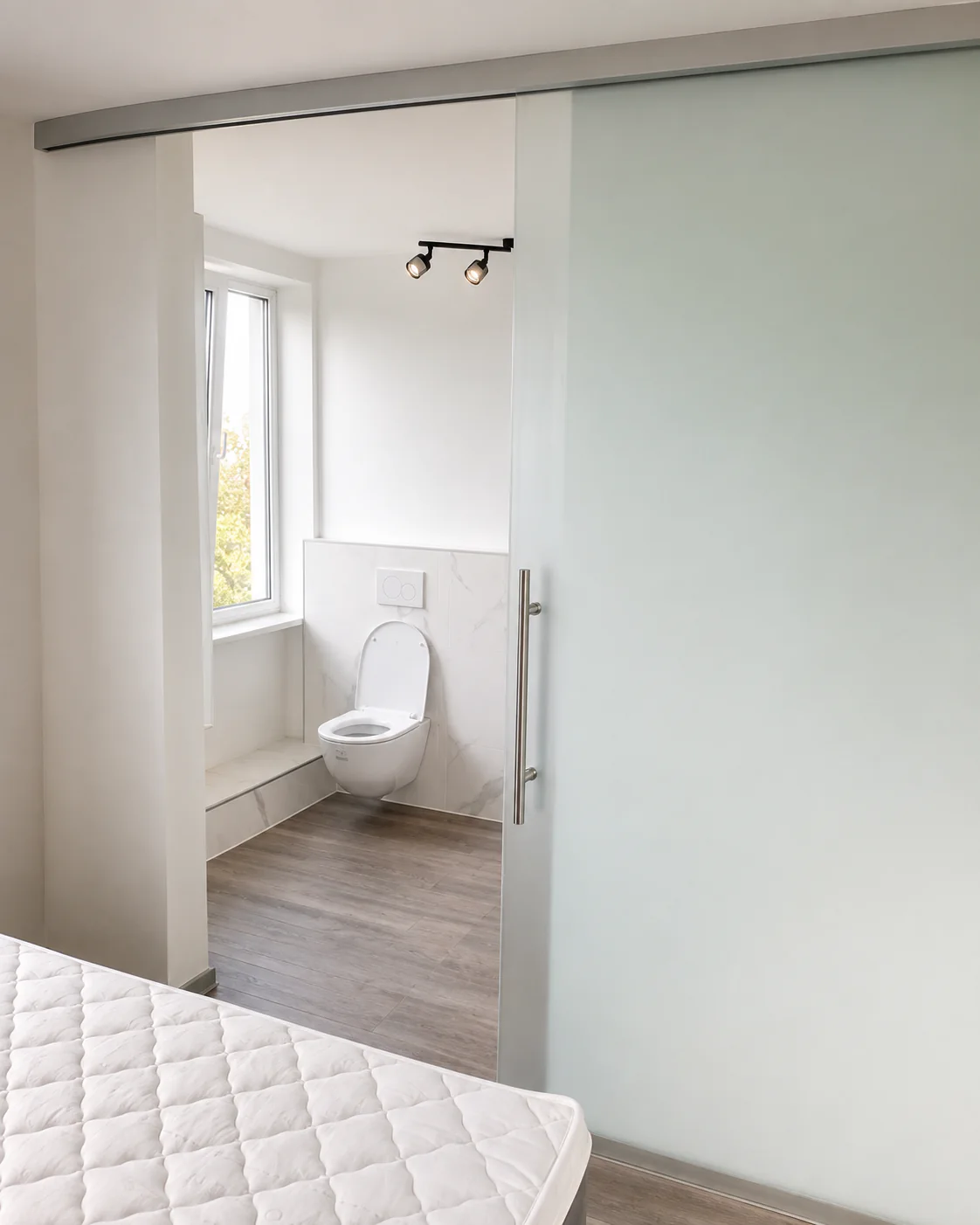 Badezimmertür aus Glas nach Maß Geöffnete Glasschiebetür zum Badezimmer nach Maß, Blick auf WC und Fenster im Bad